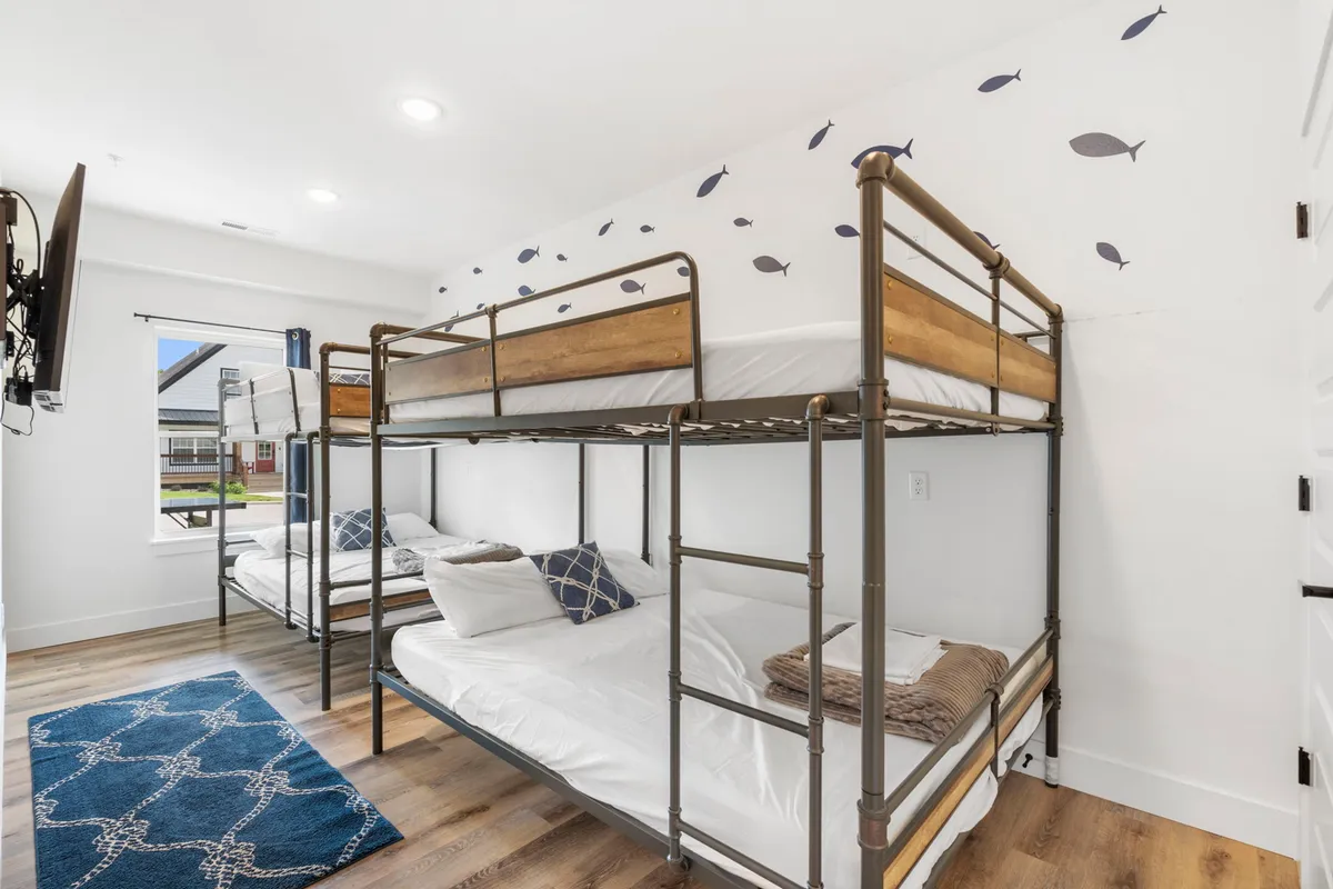 A playful bunk room with multiple bunk beds, fun fish motifs on the walls, and a cozy area rug. The space is inviting and ideal for family or group sleepovers, offering a fun and relaxed environment.