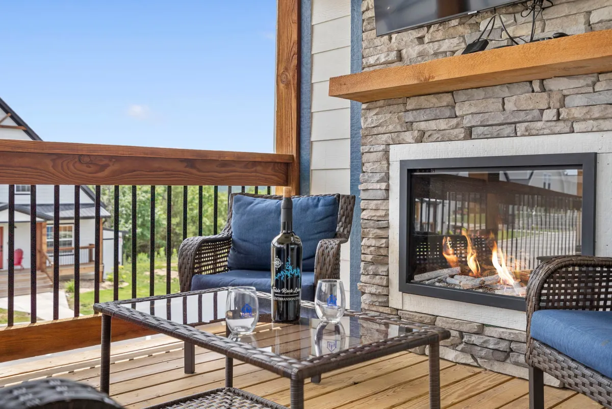 An inviting outdoor seating area centered around a crackling fireplace, with wine and comfortable chairs set against a backdrop of tranquil nature. The setting suggests warmth and relaxation during cooler evenings.