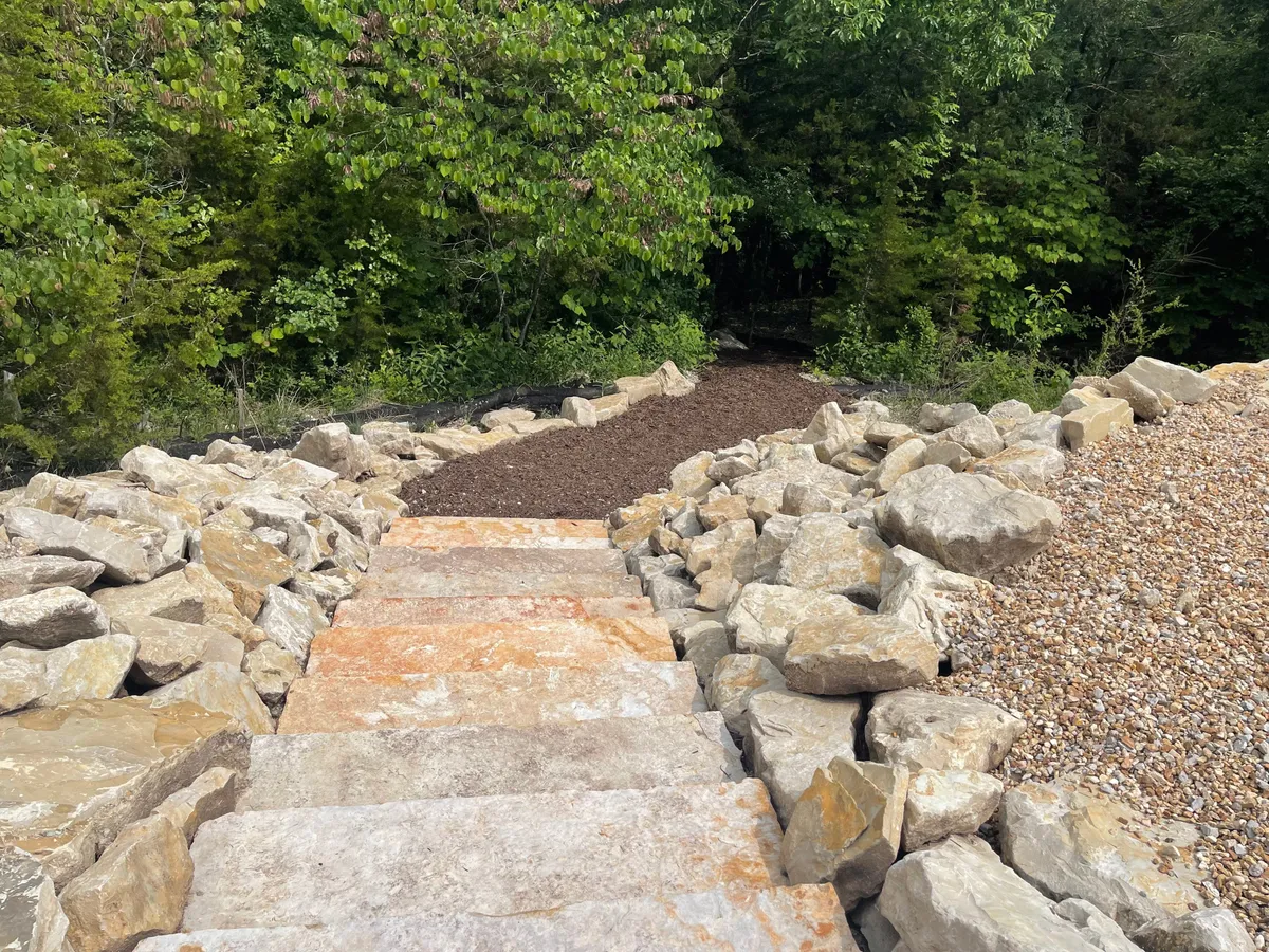 This image showcases a set of stone steps winding through lush greenery and natural rock formations. The serene pathway is inviting and hints at leisurely walks and outdoor exploration, perfect for stretching your legs with a pet. The surrounding foliage and informal path create a sense of immersion in nature, suggestive of a lakeside stroll.