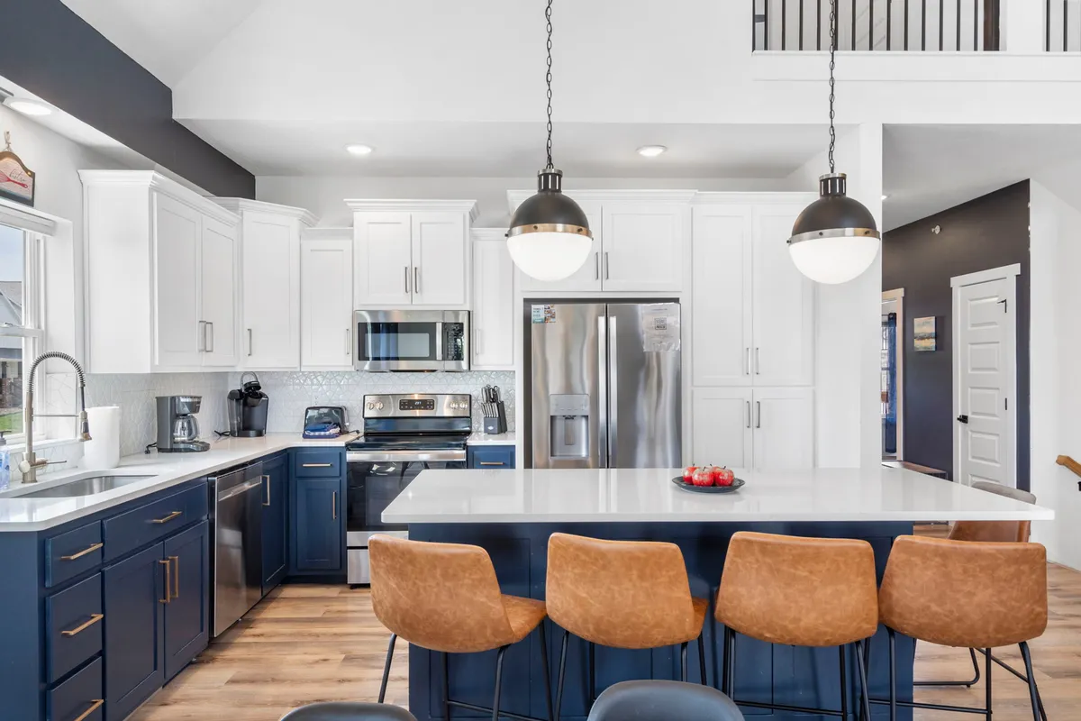 A kitchen scene displaying a large island countertop with bar stools, stainless steel appliances, and a window letting in natural light. The setup is both practical for culinary adventures and social interaction.