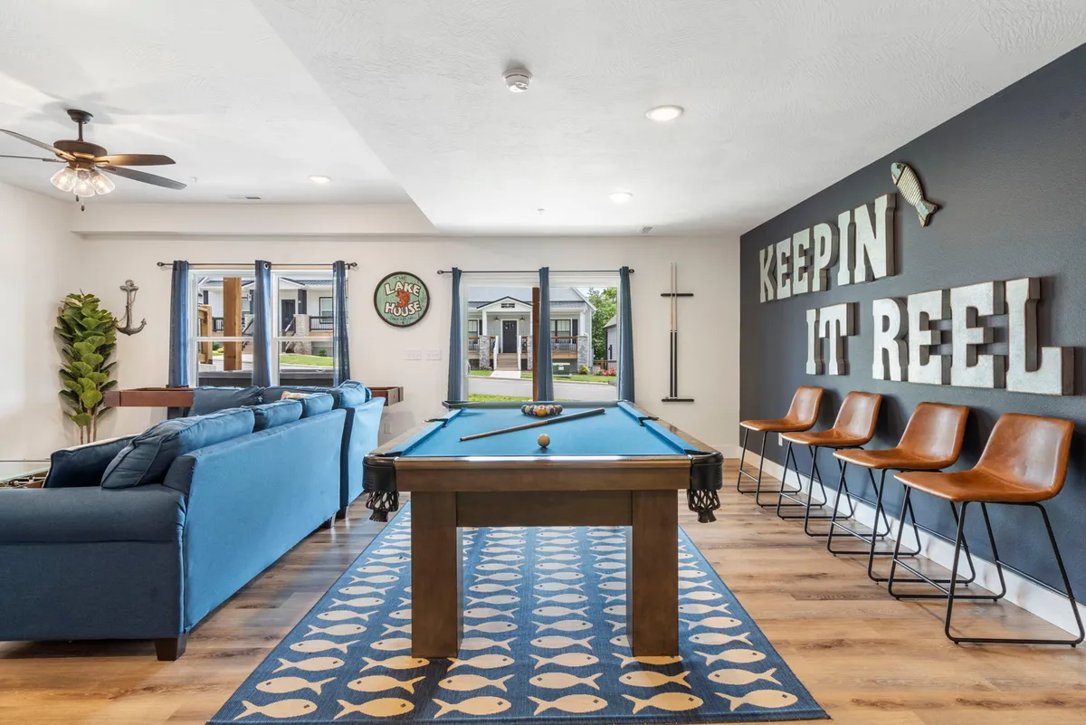 A casual and inviting recreation space with a pool table, blue couch, wall art, and bar stools. The atmosphere is energetic, perfect for friendly competitions and lively gatherings.