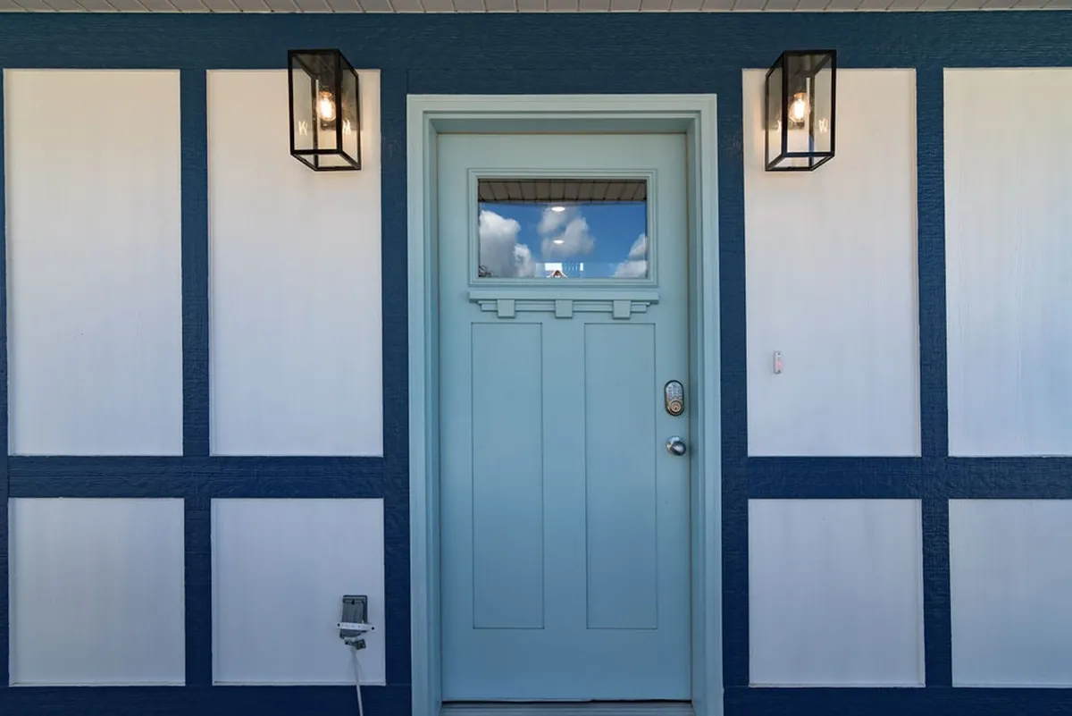 This image captures the exterior front of the home, featuring a blue front door, stylish lanterns, and contrasting wall panels. The entry is step-free and inviting, with space for greeting guests and relaxing on a porch swing.