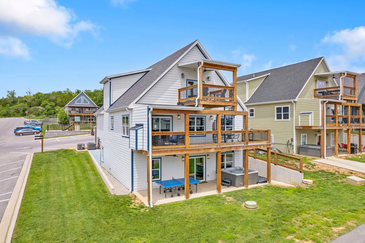 A multi-level deck offers ample outdoor seating, an inviting hot tub, and space for outdoor dining and social gatherings. The deck is surrounded by greenery and set against a backdrop of scenic views, establishing a lively but private retreat vibe.