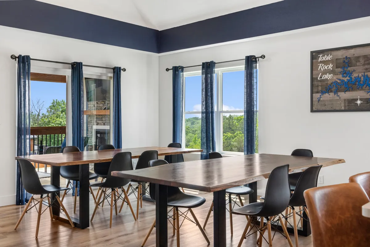 A warm dining area with large windows offering scenic views, wooden tables with stylish chairs, and wall art celebrating Table Rock Lake. The space is set for group meals or lively board games, bathed in natural light.