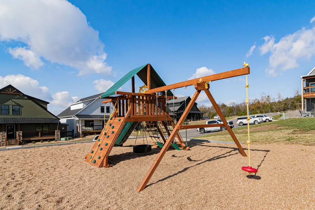 A lively playground with a swing set and surrounding homes in view. Children play and families gather, creating a joyful, energetic outdoor scene.