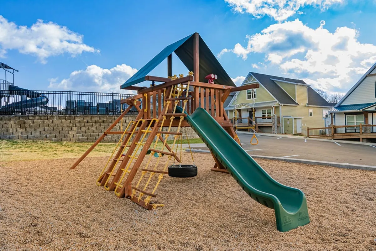 The image showcases a vibrant playground structure with a slide and swing set, set outdoors for children and families to enjoy. The area is easily accessible and ideal for multigenerational fun.