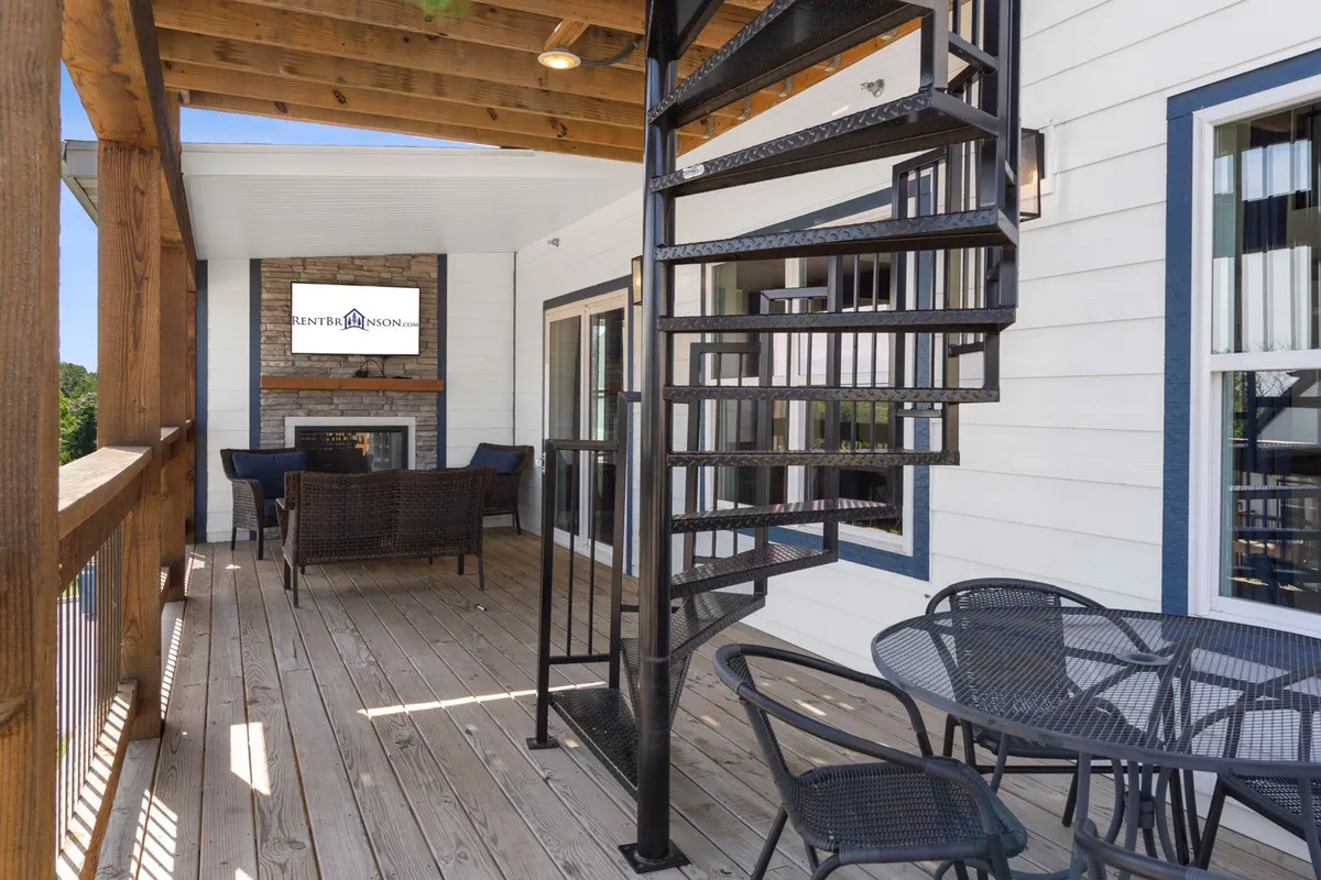 The exterior features a dramatic spiral staircase leading to a cozy outdoor fireplace area with comfortable seating. The setting is perfect for evening gatherings, fireside chats, and enjoying the outdoors after a day of fun.