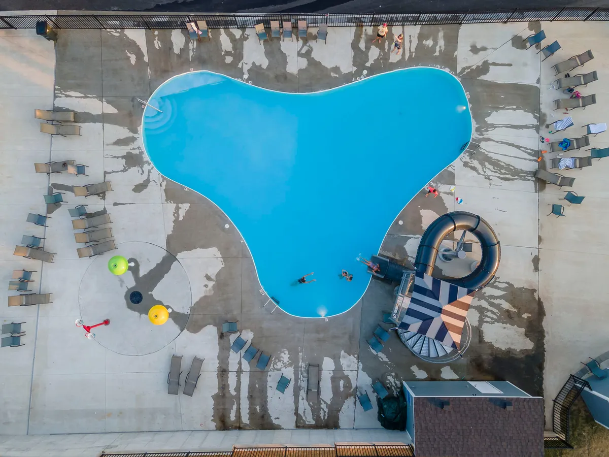 A vibrant exterior shot of the outdoor swimming pool featuring a water slide, colorful play equipment, and lounge chairs. The sunny setting and inviting atmosphere highlight the pool as a lively hub for summer fun.