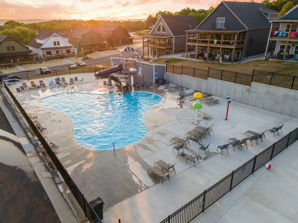 A vibrant outdoor pool scene featuring a colorful water slide, lounge chairs, and playful water features. The space buzzes with the joy of families and children enjoying the water and warm weather.