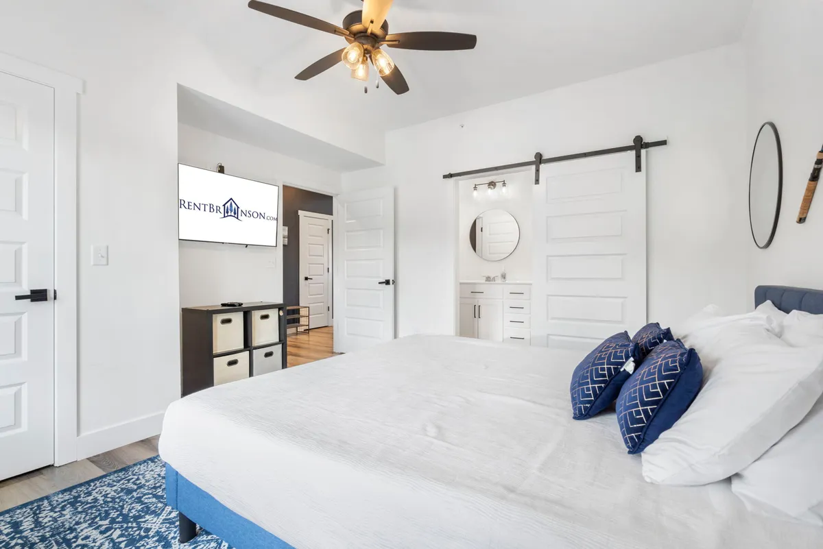 A spacious king bedroom with blue accents, a large comfortable bed, modern ceiling fan, and a wall-mounted TV displaying a logo. The room exudes a comfortable and modern ambiance, ideal for relaxing after a day of activities.