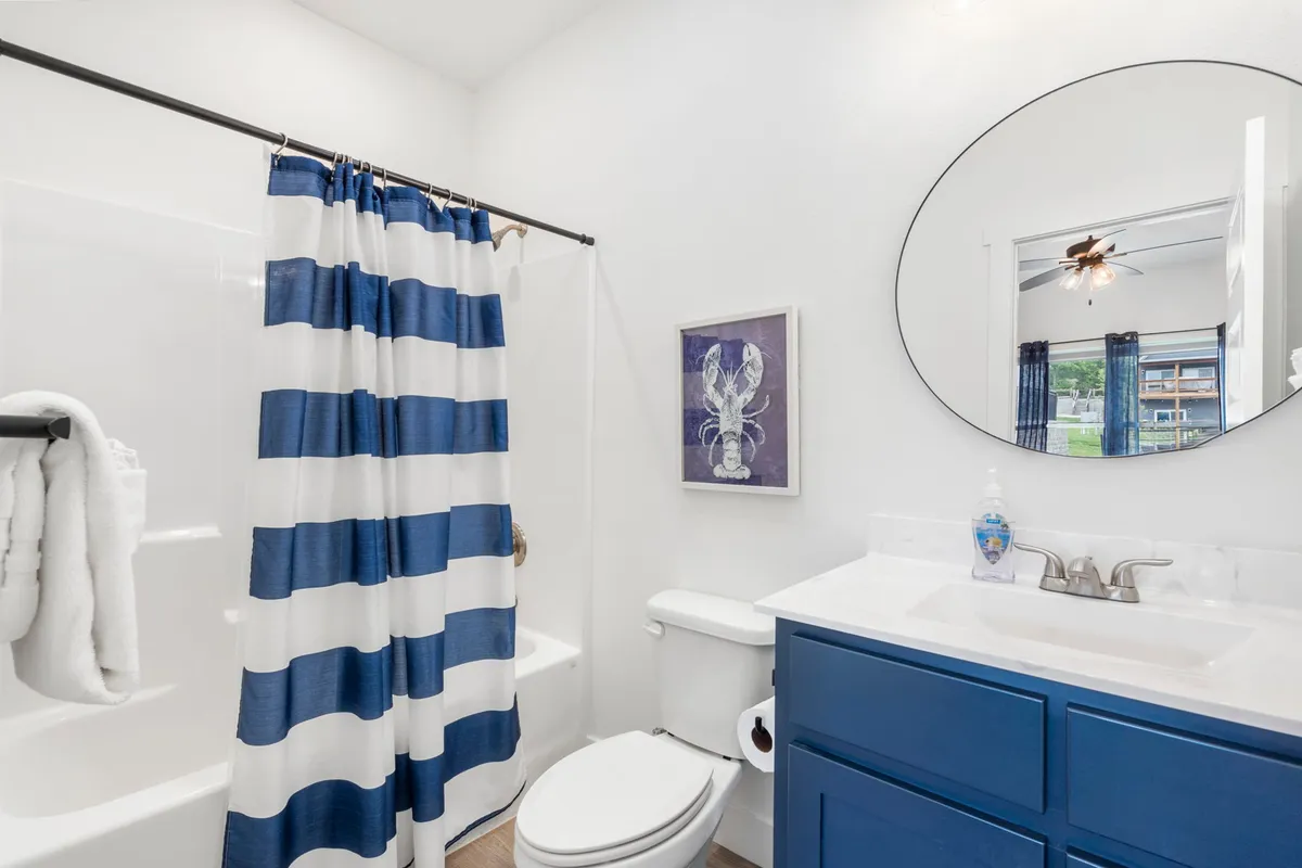 A modern bathroom with a striped shower curtain, blue vanity, and a round mirror, providing a fresh and inviting space for relaxation and self-care.