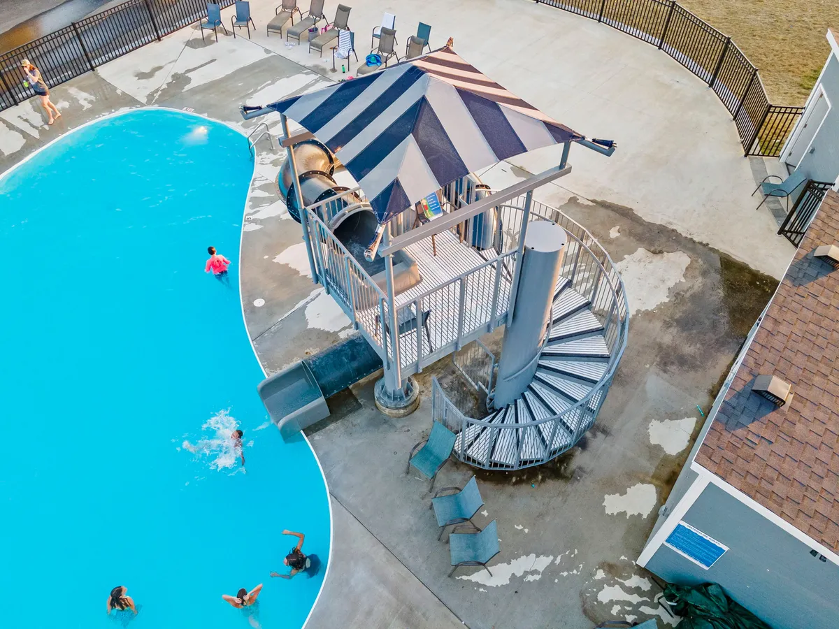 A dynamic poolside scene featuring a large outdoor swimming pool, a winding water slide, a spiral staircase, and inviting lounge chairs—ideal for both relaxation and energetic play. The atmosphere is fun and active, suggesting summer enjoyment for all ages.
