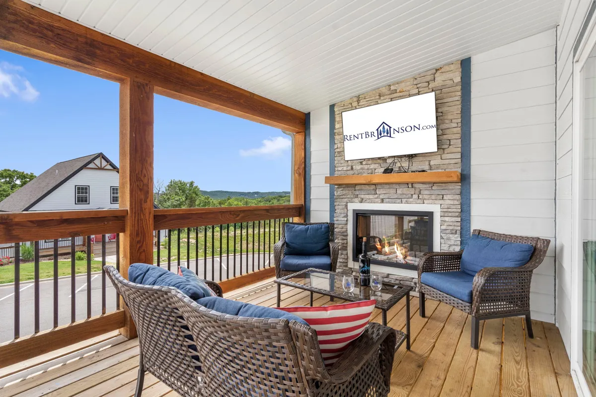 The hero image showcases the inviting exterior living area of a spacious single-family home. Comfortable seating is arranged around an elegant outdoor fireplace, perfect for gathering with friends and family. Through the railing, guests can glimpse beautiful natural surroundings, adding to the welcoming and relaxing ambiance. The space is designed for leisurely mornings with coffee, cozy evenings by the fire, and memorable celebrations.