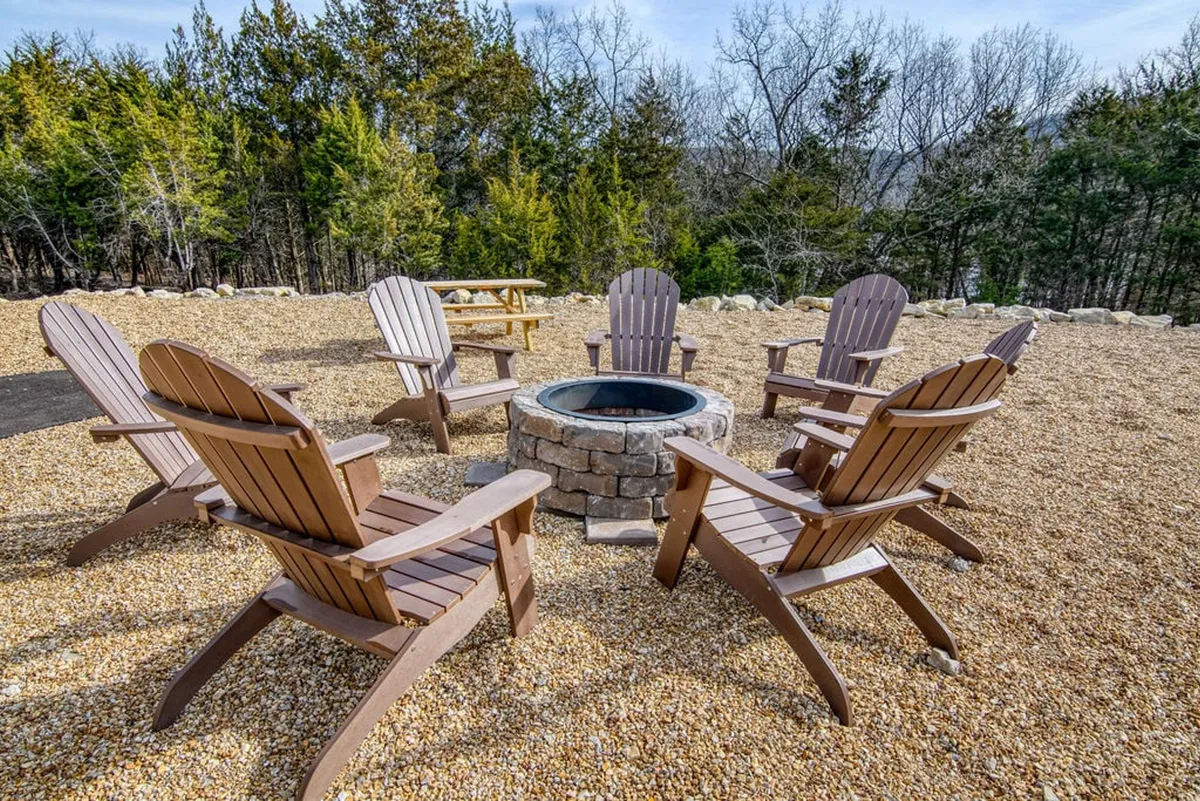 This image features a cozy outdoor fire pit surrounded by Adirondack chairs, nestled in nature. The scene suggests communal relaxation, storytelling, and making memories under the open sky—ideal for unwinding after a day of adventures with your dog.
