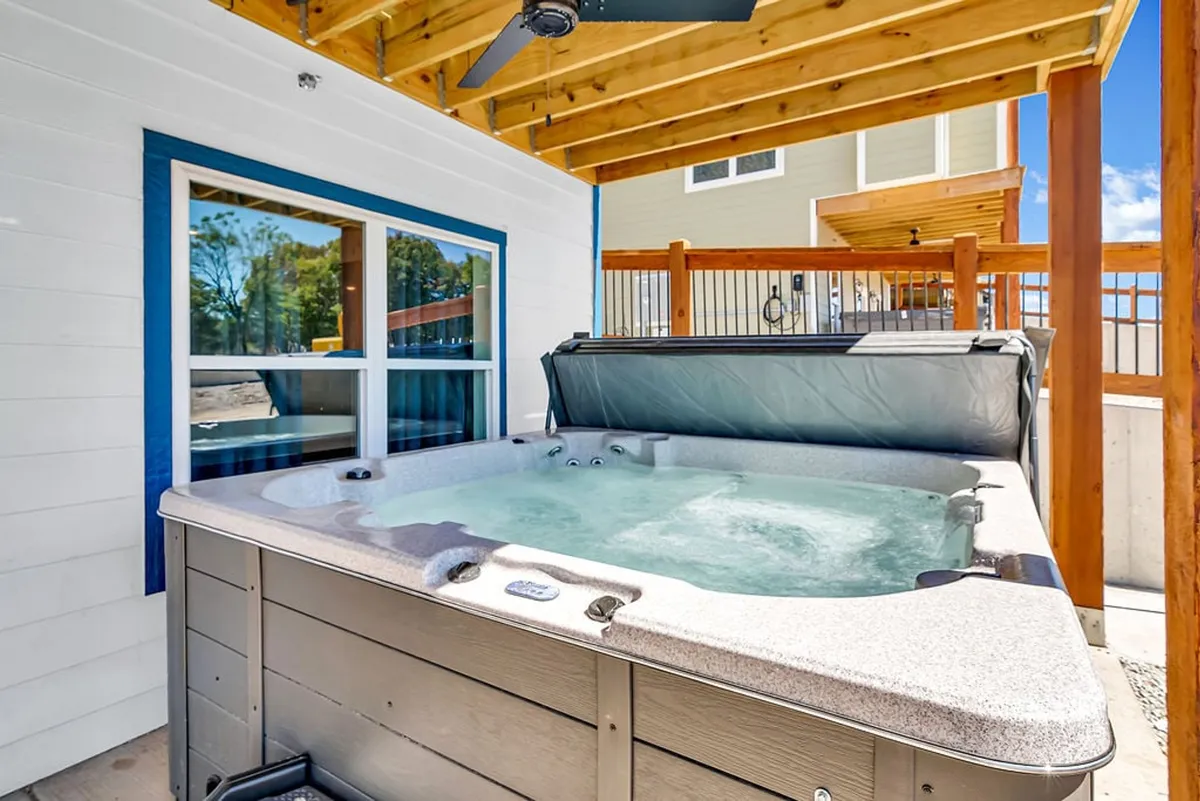 A cozy outdoor area featuring a hot tub beneath a wooden ceiling and large windows, creating an inviting spot for stargazing or socializing under the night sky.